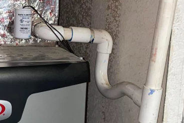 Real-world photo of a float switch installed on the PVC condensate drain line next to an indoor air handler