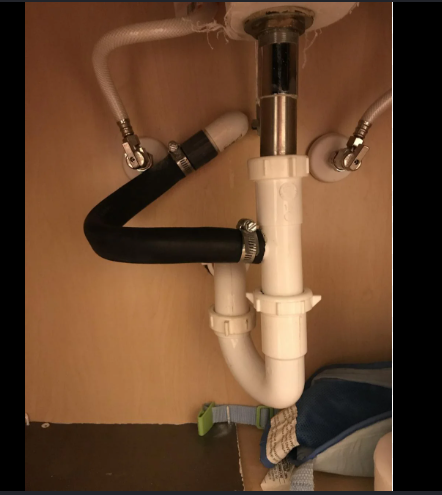 Under-bathroom-sink plumbing showing an AC condensate drain line tied into the sink P-trap with hose clamps